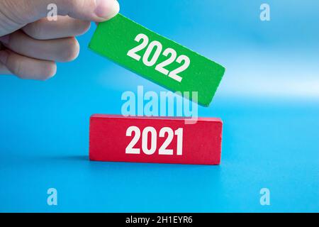New year 2022 coming concept. Woman puts the green one with 2022 on top of the red wooden block with 2021 on it. 2021 ends and new year 2022 begins.