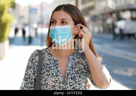 Girl in the street puts on a medical mask. Young business woman wearing surgical mask walking in city street. Stock Photo