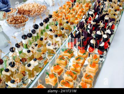Closeup of small canapes for catering arranged on a mirror plates. Buffet table with cold appetizers and aperitifs with cheese and caviar. Concept of Stock Photo