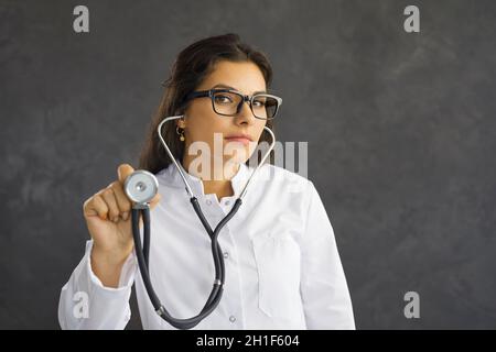 Young serious female healthcare worker holding a stethoscope extended towards the viewer. Stock Photo