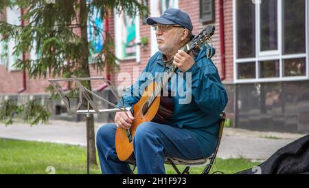 02/06/2020: A street musician plays guitar music for people passing by. An elderly man with a guitar on the street plays popular music for the public. Stock Photo