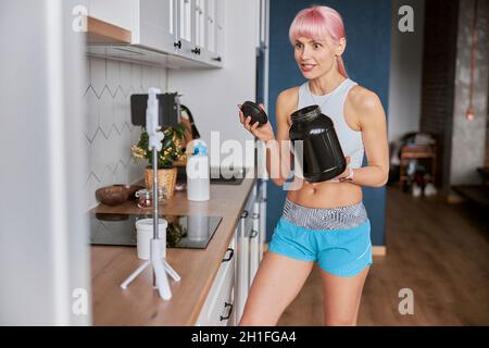 Excited woman shows large jar of dietary supplement shooting to camera in kitchen Stock Photo