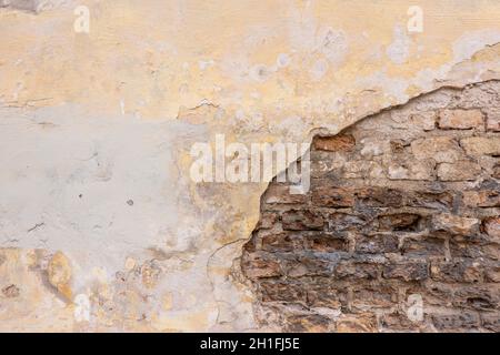 Old cracked weathered shabby yellow painted plastered peeled brown brick wall background Stock Photo