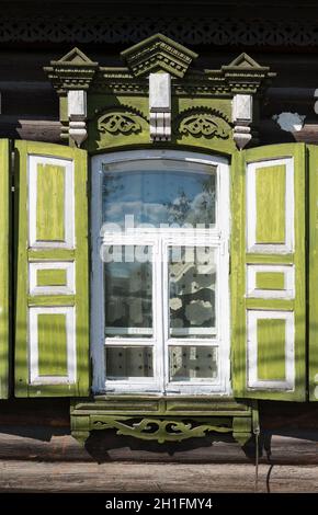 Floral pattern curtainig  behind a window with green shutters of  a traditional wooden house in Ulan-Ude. Republic of Buryatia, Russia Stock Photo