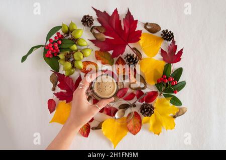 Coffee cup on a background of yellow and red autumn leaves with a woman's hand Stock Photo
