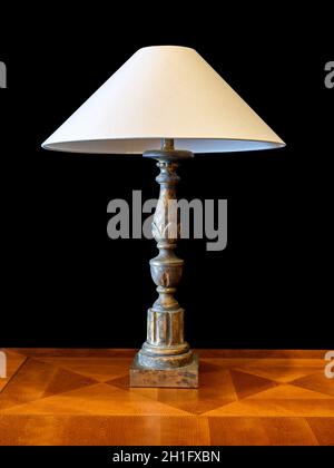 old brass patina lamp with fabric lampshade, on brown wood with geometric veneer. Isolated on black background, clipping path attached Stock Photo