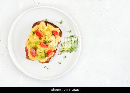 Scrambled eggs with microgreen and tomatoes on bread over light  stone background with free text space. Top view, flat lay Stock Photo