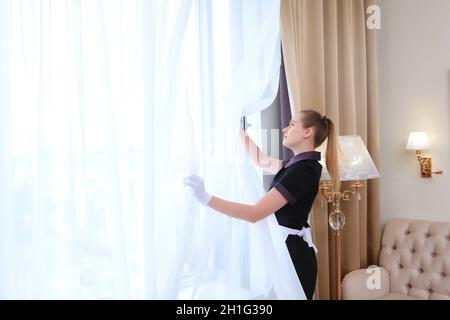 A woman in a cleaning service uniform ventilates the living room. Hygiene inside an apartment or house. Photo in the interior. The concept of cleanlin Stock Photo