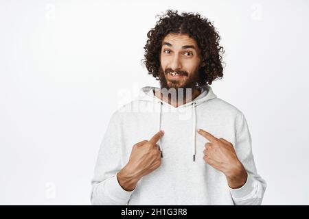 Portrait of surprised hispanic man pointing fingers at himself with questioned face, who me gesture, white background Stock Photo