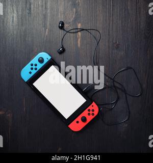 Minsk, Belarus - May 07, 2020: Nintendo Switch game console with white screen and bright joy-con controllers and headphones on vintage wood table back Stock Photo
