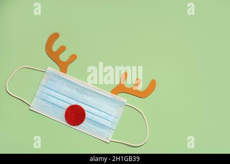 Merry Christmas.Christmas concept background.Christmas Rudolph reindeer horns with protective surgical mask over green background Stock Photo