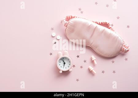 Female eye mask, alarm clock, earplugs, pills on pink background with confetti. Insomnia treatment concept. Stock Photo