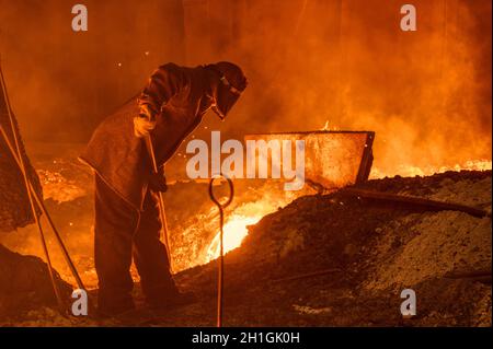 The process of releasing pig iron from a blast furnace. A man works with molten metal Stock Photo