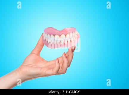 Female hand and false prosthese. Dental hygienist checkup concept. Full removable plastic denture of the jaws. Stock Photo