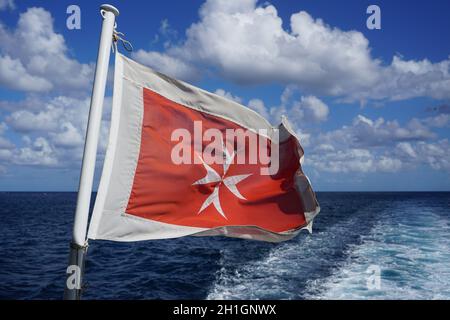 Old Maltese flag. White cross on red background flying at stern of ship travelling in the Mediterranean Sea.Photo by Willy Matheisl Stock Photo