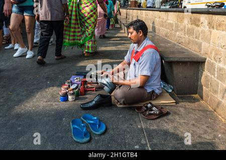 Mumbai, India - November 22, 2019: Poor shoe shiner siting on the floor and cleans shoes near Gateway of India in Mumbai (colloquially known as Bombay Stock Photo