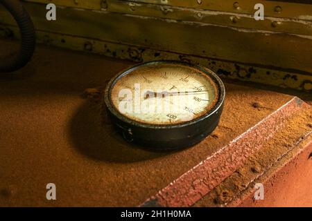 Old industrial circular thermometer gauge showing high temperature, on top of oven used to dry tea, covered with brown tea dust. Stock Photo