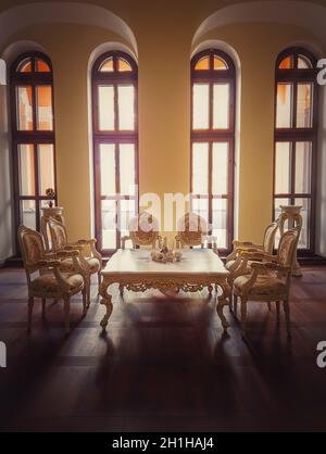 Ancient royalty dining room, medieval furniture style with golden ornate chairs and table near the arched windows. Luxury hosting room background, old Stock Photo