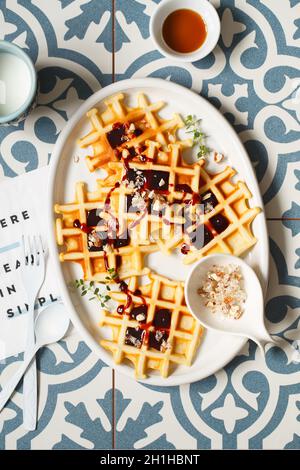 Belgian or Brussels waffles with date syrup or jam and candied roasted nuts. Homemade waffles in a white oval Plate on the kitchen table. Traditional Stock Photo