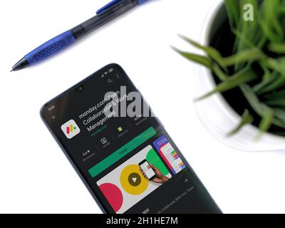 Lod, Israel - July 8, 2020: Modern minimalist office workspace with black mobile smartphone with Monday app play store page on white background. Top v Stock Photo