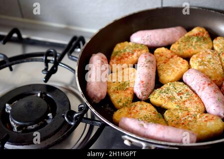 Cooking process with sausages and hash browns covered in spices and paprika in frying pan on gas stove. Stock Photo