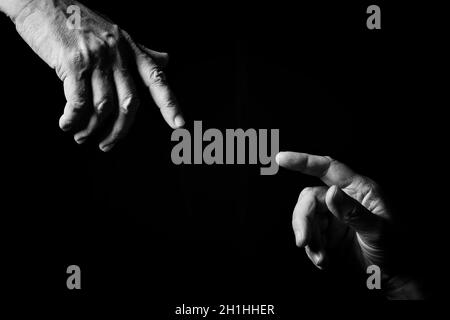 Black & white image of two male hands pointing or touching, as Creation of Adam, isolated against a black background with dramatic lighting. Stock Photo