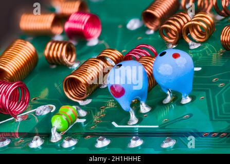 Orange and red radio-frequency coils or blue tantalum capacitors on printed circuit board. Closeup of air core inductors soldered on green TV card PCB. Stock Photo