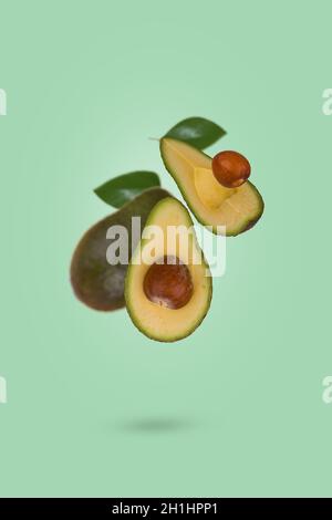 Creative scene with fresh ripe whole and sliced avocado flying in air isolated on  light green background. Healthy food, diet, tropical exotic fruit, Stock Photo