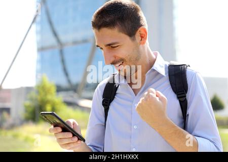 Portrait of excited young business man checking good news on smartphone. University student celebrating with mobile phone in his and in modern city st Stock Photo