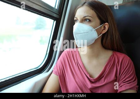 Travel safely on public transport. Young woman with KN95 FFP2 face mask looking through train window. Train passenger with protective mask. Stock Photo