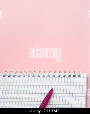 A blank checkered sheet of paper. Notepad and pen on pink. Pink Pen. Notepad spring Spiral spiral checked sheets. Stock Photo