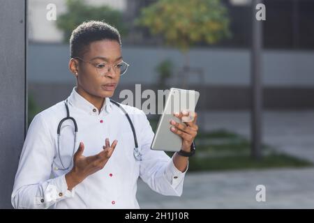 Female doctor conducts an online consultation via video link holding a tablet, near the clinic, a conference at lunchtime with staff Stock Photo