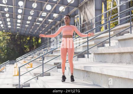 Woman doing burpee exercise, young African American woman doing fitness and active lifestyle in the morning, outdoors near the stadium Stock Photo