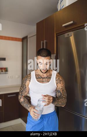 Hot tattoed man drinking water in the kitchen Stock Photo