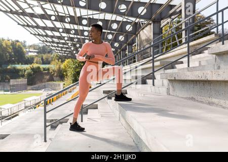 Female athlete doing fitness in a pink sports suit near the sports stadium, African American performs fitness exercises and stretching in the morning Stock Photo