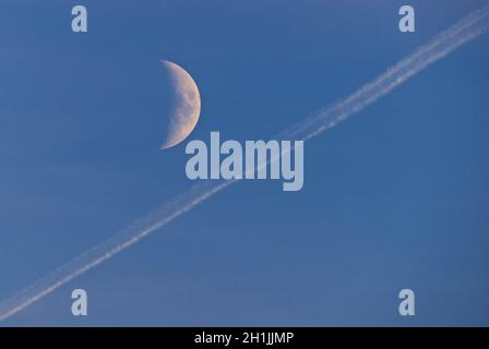 The moon (half crescent) and an aviation contrail in a clear blue sky. Stock Photo