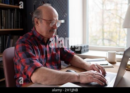 Senior man at home in front of laptop computer Stock Photo