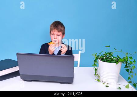 A boy in a school suit with food in his hands, copy space on a blue studio background Stock Photo