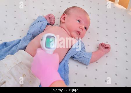 Doctor checks the temperature of the newborn baby with a thermometer. A nurse in uniform measures the child fever with a thermometer Stock Photo