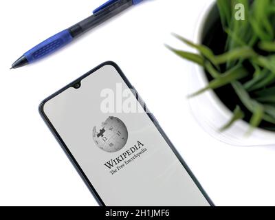 Lod, Israel - July 8, 2020: Modern minimalist office workspace with black mobile smartphone with Wikipedia app launch screen with logo on a white back Stock Photo