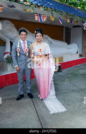 Portrait, in front of a statue of Buddha. of Thai bride & her South American groom just after their Buddhist wedding In Elmhurst, Queens, New York. Stock Photo