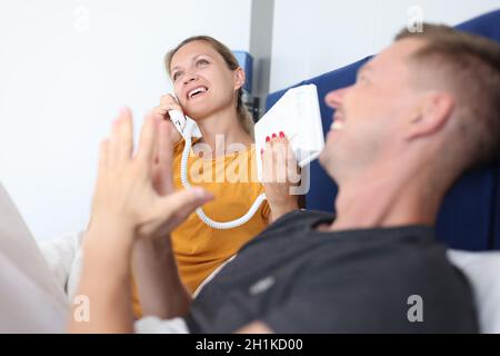 Woman is talking on phone while lying with man on bed in hotel room Stock Photo