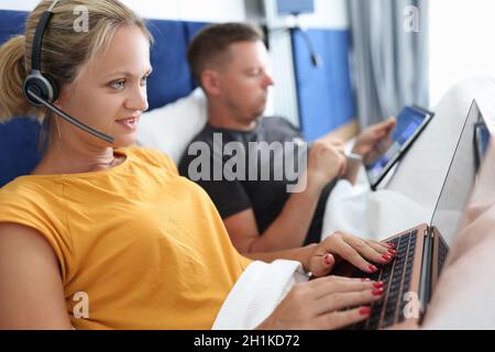Young couple man and woman work remotely on laptop while lying in bed Stock Photo