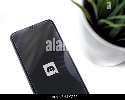 Lod, Israel - July 8, 2020: Modern minimalist office workspace with black mobile smartphone with Discord app launch screen with logo on white backgrou Stock Photo