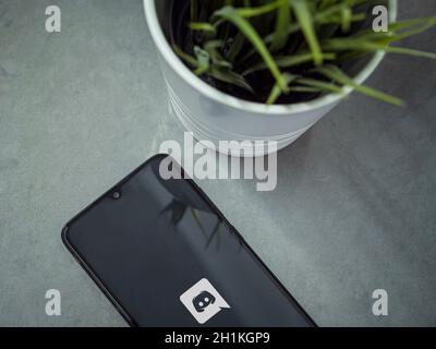 Lod, Israel - July 8, 2020: Modern minimalist office workspace with black mobile smartphone with Discord app launch screen with logo on marble backgro Stock Photo