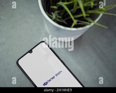 Lod, Israel - July 8, 2020: Modern minimalist office workspace with black mobile smartphone with Israel Railways app launch screen with logo in hebrew Stock Photo