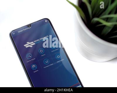 Lod, Israel - July 8, 2020: Modern minimalist office workspace with black mobile smartphone with Israel Railways app launch screen with logo on white Stock Photo