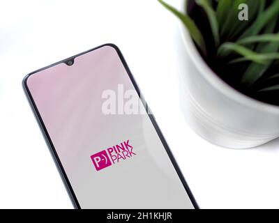 Lod, Israel - July 8, 2020: Modern minimalist office workspace with black mobile smartphone with Pink Park app launch screen with logo on white backgr Stock Photo