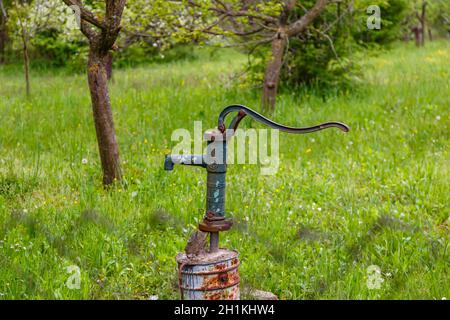 Image of an outdoor water faucet placed on a rusty bucket in a garden. Stock Photo