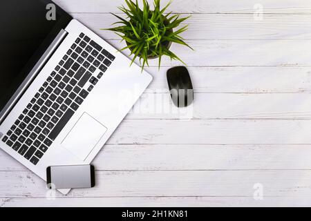Working place on white wooden table with copy space. Laptop, mouse, phone, flower in a pot. Flat lay. Top view of blackboard office desk Stock Photo